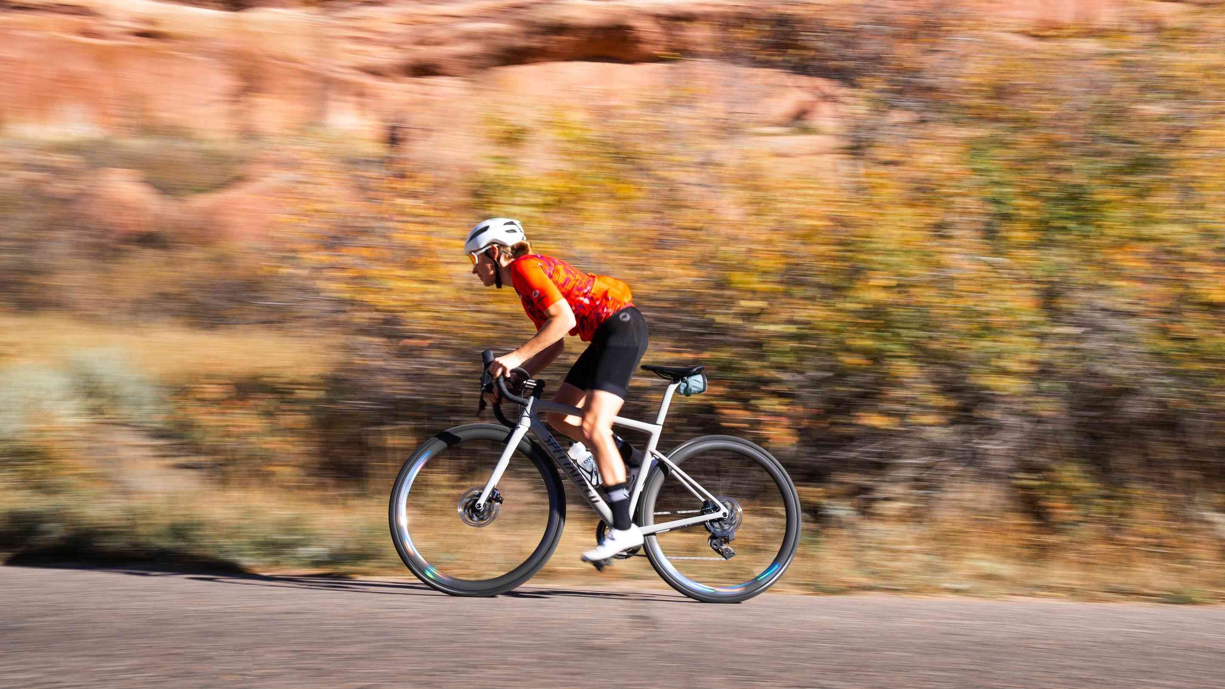 Female cyclist wearing a bright orange cycling jersey and black cargo cycling bib shorts