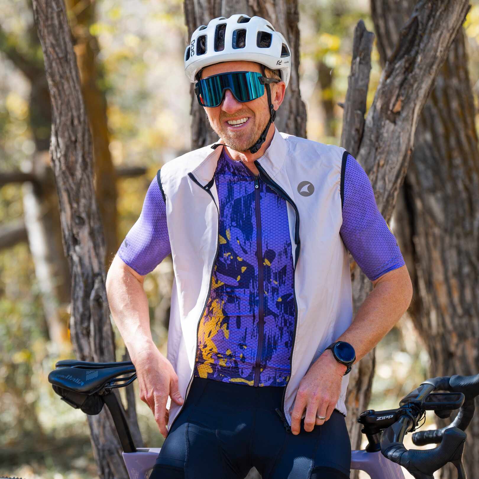 Male cyclist wearing bright purple mesh cycling jersey and a grey cycling wind vest 